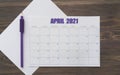 Event planner for April 2021. Calendar page on white paper, next to purple pencil. Brown wooden background. Table with the days