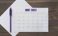 Event planner for MAY 2021. Calendar page on white paper, next to purple pencil. Brown wooden background. Table with the days and