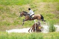 Eventing: equestrian rider jumping over an a log fence water obstacle