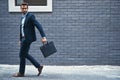 Every businessman needs a briefcase. a handsome young businessman carrying a briefcase against a grey facebrick wall.