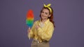 Woman in casual clothing posing at the camera, holding colorful pipidaster brush in hands, pointing at it. Isolated on