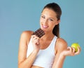 Everything in moderation. Studio shot of a fit young woman holding an apple and a chocolate against a blue background.