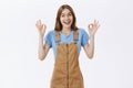 Everything okay, chill. Friendly and enthusiastic good-looking female in brown overalls showing ok gesture and smiling