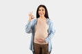 Everything is okay. Happy young pregnant lady gesturing okay and touching belly, looking and smiling at camera