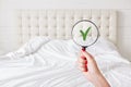 Everything in perfect and clean. Woman checks condition in hotel room, holds lens against white bed which demonstrates purity and Royalty Free Stock Photo