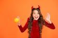 Evil demon. Little demon of child orange background. Happy girl with red demon horns hold pumpkin. Demon is ghouls best