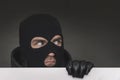 An evil thief in mask looks out from behind a white board. Space for text and design. copy space. surprised bandit looks Royalty Free Stock Photo