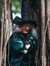 Evil witch on nature dark background, closeup portrait of old lady with terrifying makeup, Halloween background