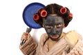 Evil young housewife in curlers and cosmetic face mask holding a frying pan