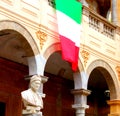 Italian flag hanging from a building with the bust of Dante in the foreground