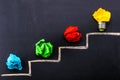 Evolving idea concept with colorful crumpled paper and light bulb on steps drawn on blackboard Royalty Free Stock Photo