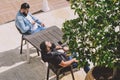 Two black-haired men with beards sit at a table in a street cafe and sunbathe