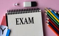 EXAM - a word written in a notebook on a pink background and colored pencils Royalty Free Stock Photo