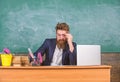 Examiner full of doubts sit at table chalkboard background. School exam concept. Examiner bearded teacher with