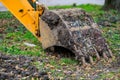 Excavator bucket in muddy park setting with green grass and leaves Royalty Free Stock Photo