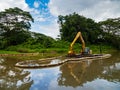 An excavator / bulldozer performing dredging work in a canal / river in a tropical rainforest / jungle habitat in Singapore, South