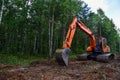 Excavator clearing forest for new development. Orange Backhoe modified for forestry work. Tracked heavy power machinery for forest