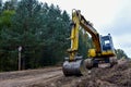 Excavator during construction new road in forest area. Yellow backhoe at groundwork. Earth-moving equipment fort road work,