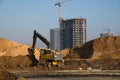 Excavator at a construction site on a background of a construction cranes and building. Backhoe dig the ground for the foundation