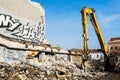 Excavator demolishing old building which walls with graffiti in day time