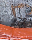 The excavator destroys the old wooden house on the background of snow-covered trees and new buildings. The winter. Royalty Free Stock Photo