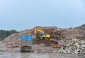 Excavator dig construction waste at landfill. Truck with metal tank and capacitie for storage and transportation of garbage at MSW