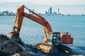 Excavator or digger working on earthmoving at shore protection works in Batumi. Orange backhoe digs sand and gravel