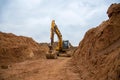 Excavator digs a large trench for pipe laying. Backhoe during earthmoving at construction site. Earth-moving heavy equipment Royalty Free Stock Photo