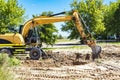 An excavator digs a pond pit in the garden against the blue sky. Digging a pit with an excavator. Earthmoving equipment and Royalty Free Stock Photo