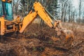 The excavator digs soil into the forest and uproots the roots of the trees