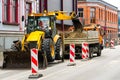 An excavator digs a trench on street and pours earth in a truck