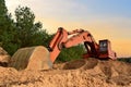 Excavator on earthworks against the background of sunset in a forest area. Illegal forest clearing to develop open pit for sand