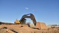 Excavator on earthworks at construction site. Backhoe on foundation work and road construction. Tower cranes in action on blue sky Royalty Free Stock Photo