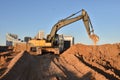 Excavator on earthworks at construction site. Backhoe on foundation work and road construction. Tower cranes in action on blue sky Royalty Free Stock Photo