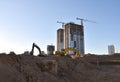 Excavator on earthworks at construction site. Backhoe on foundation work and road construction. Tower cranes in action on blue sky Royalty Free Stock Photo