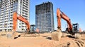 Excavator on earthworks at construction site. Backhoe on foundation work and road construction. Tower cranes in action on blue sky Royalty Free Stock Photo