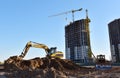 Excavator on earthworks at construction site. Backhoe on foundation work and road construction. Tower cranes in action on blue sky Royalty Free Stock Photo