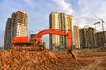 Excavator during excavation at construction site on sunset background. Red Backhoe on road work. Heavy Construction Equipment for