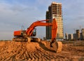 Excavator during excavation at construction site on sunset background. Red Backhoe on road work. Heavy Construction Equipment for Royalty Free Stock Photo