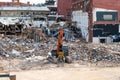 An excavator in front of a pile of debris from a destroyed building