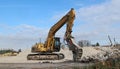 An excavator in front of a pile of rubble during an urban redevelopment. In the background two telescopic cranes