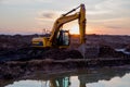 Excavator at lake in the quarry on sunset background. Backhoe during earthmoving work at open-pit mining. Earth-moving Royalty Free Stock Photo