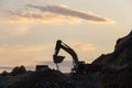 Excavator loading soil into a dump truck at dusk during road construction, creating a dramatic silhouette against the evening sky Royalty Free Stock Photo