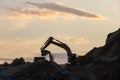 Excavator loading soil into a dump truck at dusk during road construction, creating a dramatic silhouette against the evening sky Royalty Free Stock Photo