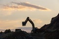 Excavator loading soil into a dump truck at dusk during road construction, creating a dramatic silhouette against the evening sky Royalty Free Stock Photo