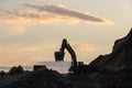 Excavator loading soil into a dump truck at dusk during road construction, creating a dramatic silhouette against the evening sky Royalty Free Stock Photo