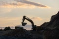 Excavator loading soil into a dump truck at dusk during road construction, creating a dramatic silhouette against the evening sky Royalty Free Stock Photo