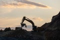 Excavator loading soil into a dump truck at dusk during road construction, creating a dramatic silhouette against the evening sky Royalty Free Stock Photo