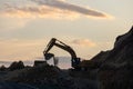 Excavator loading soil into a dump truck at dusk during road construction, creating a dramatic silhouette against the evening sky Royalty Free Stock Photo