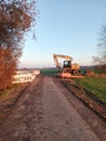 Excavator near little road and farming fields Royalty Free Stock Photo
